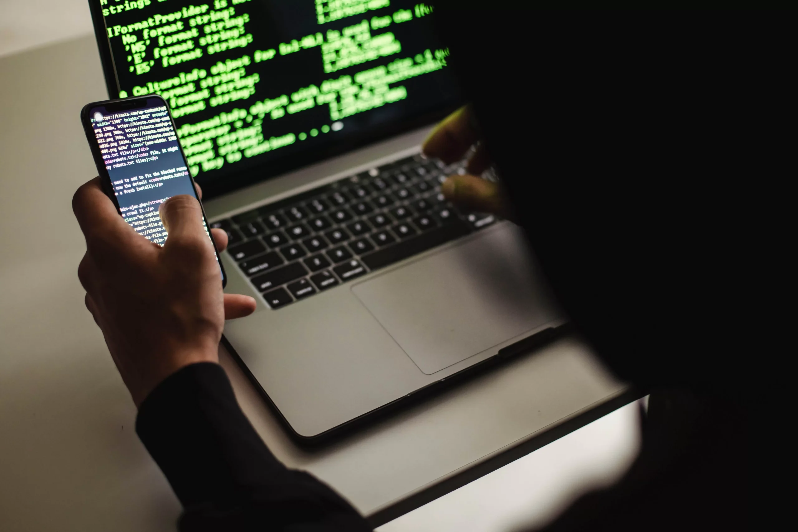 Developer using a laptop and a smartphone simultaneously to code.