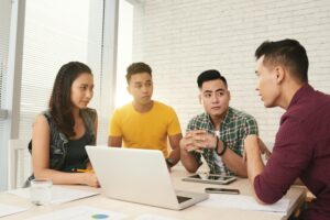 A group of Filipinos wearing semi-casual attire brainstorming in an office around a laptop.