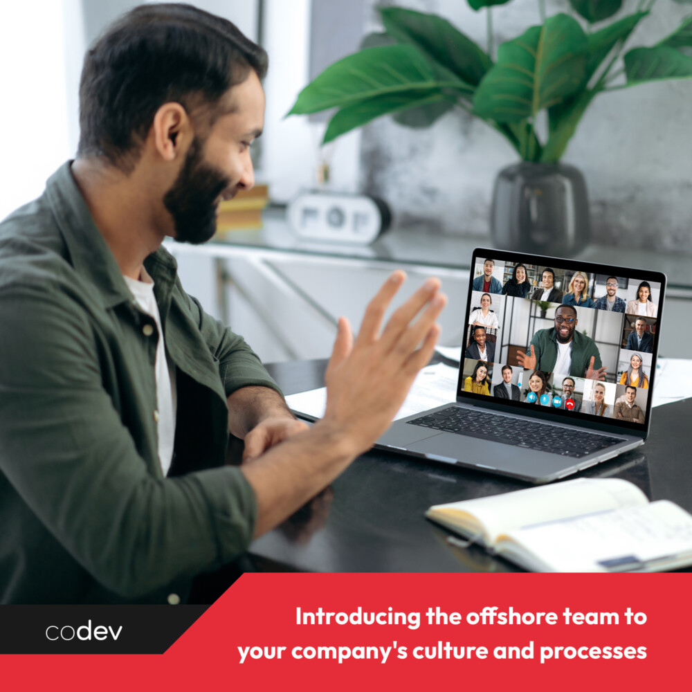 An adult man on a virtual meeting, waving his right hand to greet the members.