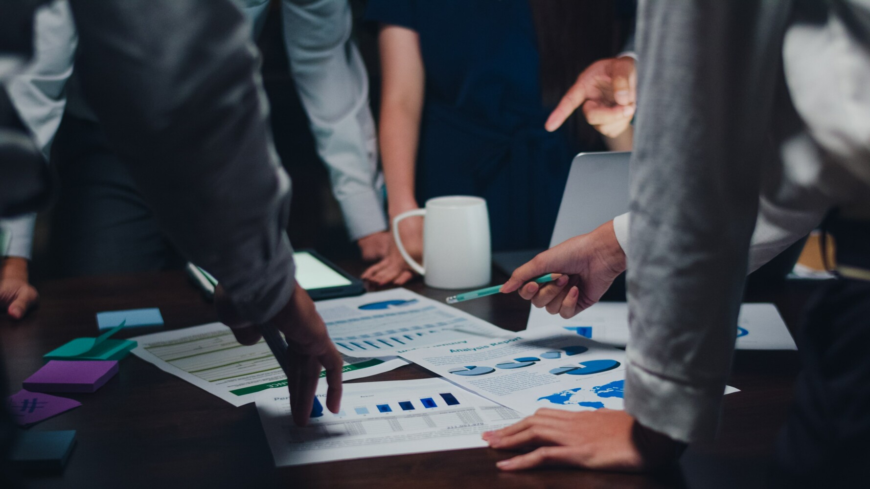 A group of corporate workers gathered around documents discussing stats and numbers.