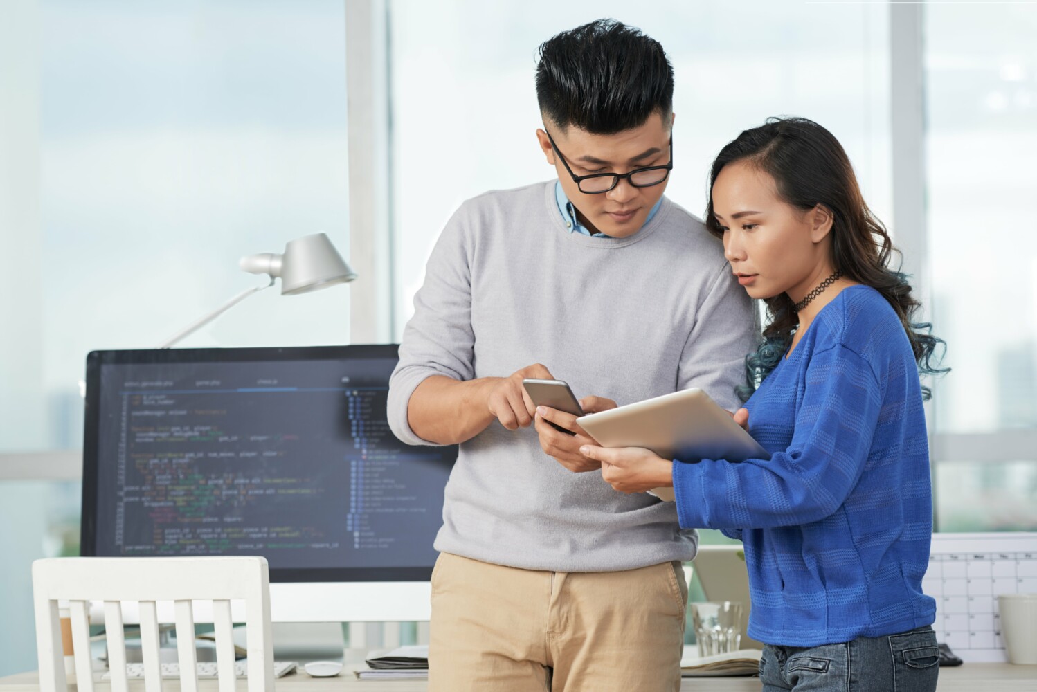 Two Asian employees looking at documents at an office discussing metrics.